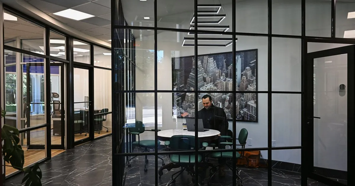 Frente interior de oficinas en vidrio con perfilería negra en cuadrícula y piso oscuro tipo mármol