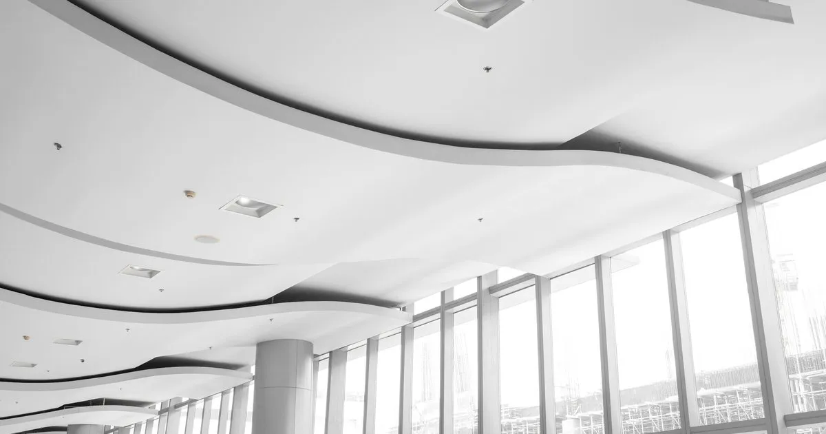 Cielo raso en drywall con formas curvas en varios niveles y luces empotradas en un salón amplio con ventanales