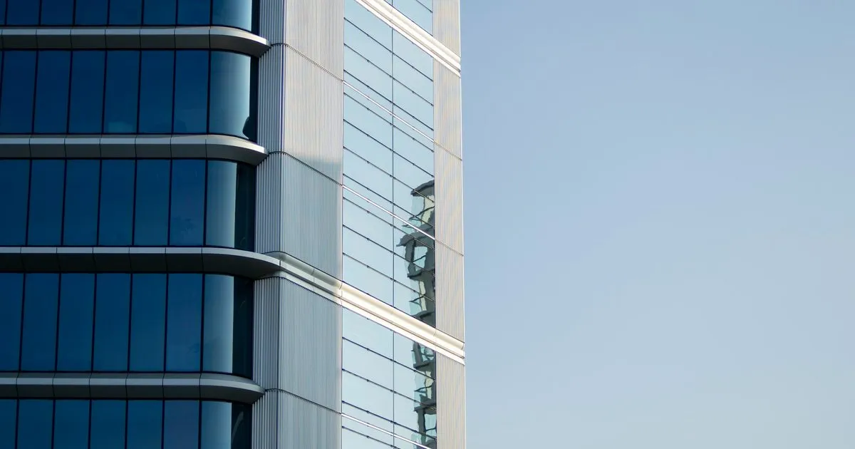 Esquina de un edificio con fachada continua de vidrio azul oscuro y perfilería de aluminio contra un cielo despejado
