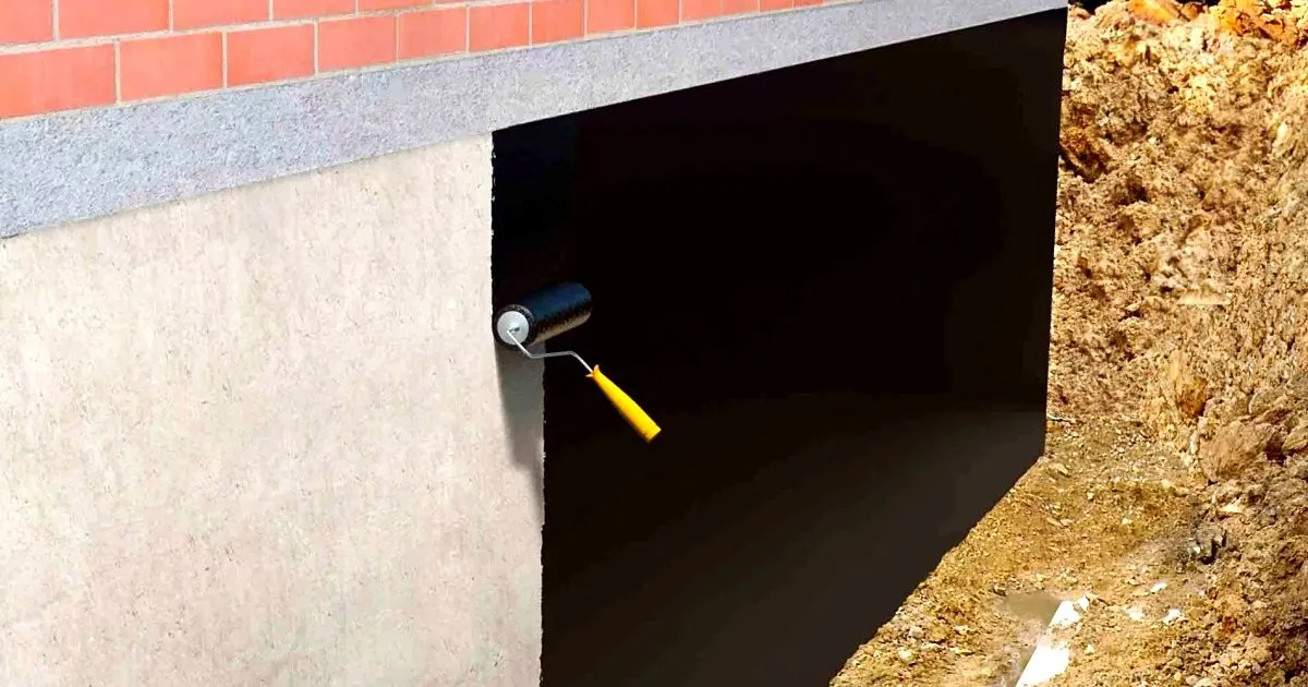 Rodillo aplicando recubrimiento negro sobre un muro de concreto al borde de una excavación