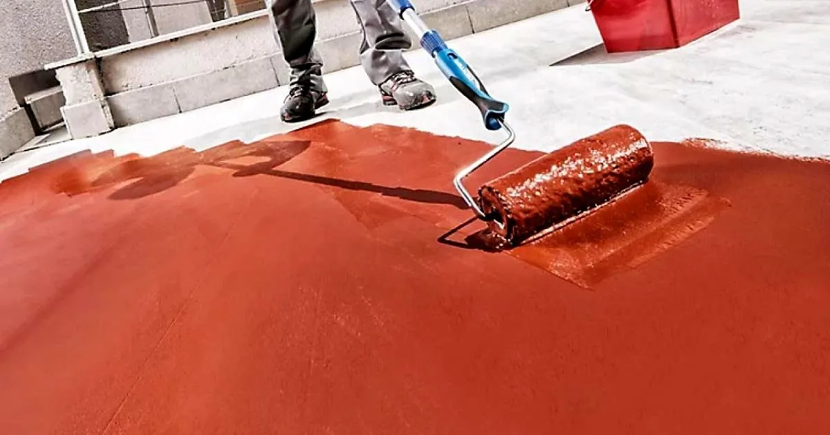 Operario aplicando con rodillo un impermeabilizante líquido de color rojo sobre el piso de una terraza