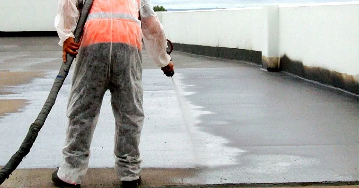 Aplicador con overol protector proyectando poliurea con pistola y manguera sobre una cubierta de concreto