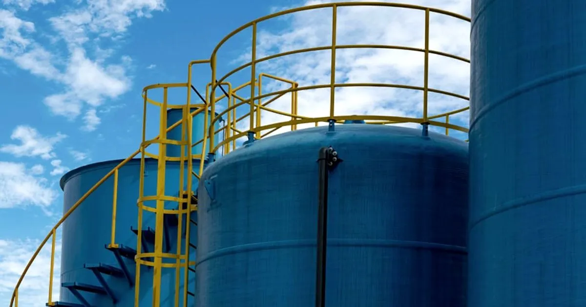 Tanques cilíndricos azules de almacenamiento con escalera y barandas amarillas bajo un cielo con nubes