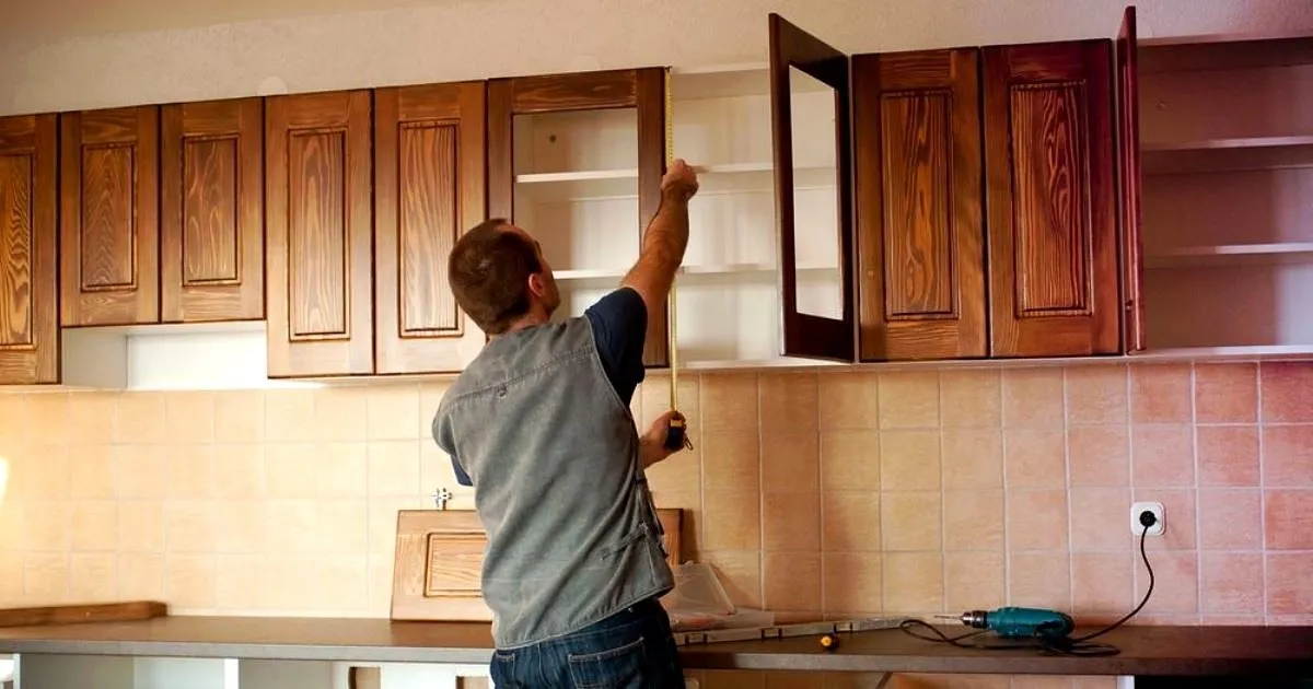 Instalador de espaldas midiendo con flexómetro los muebles altos en madera de una cocina integral