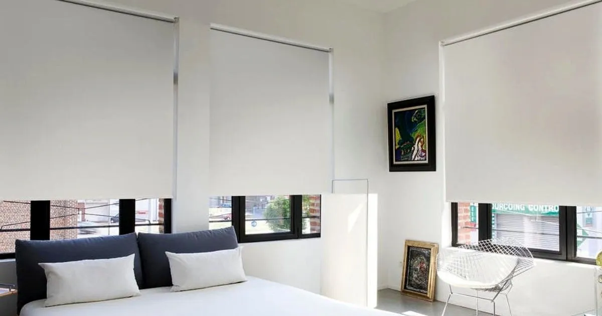 Habitación con tres cortinas enrollables blackout blancas instaladas a media altura sobre ventanas de marco negro