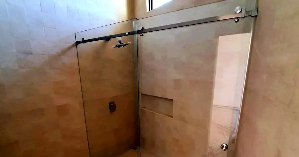 División de baño corrediza en vidrio templado con barra superior en acero, en una ducha enchapada en tono beige con nicho