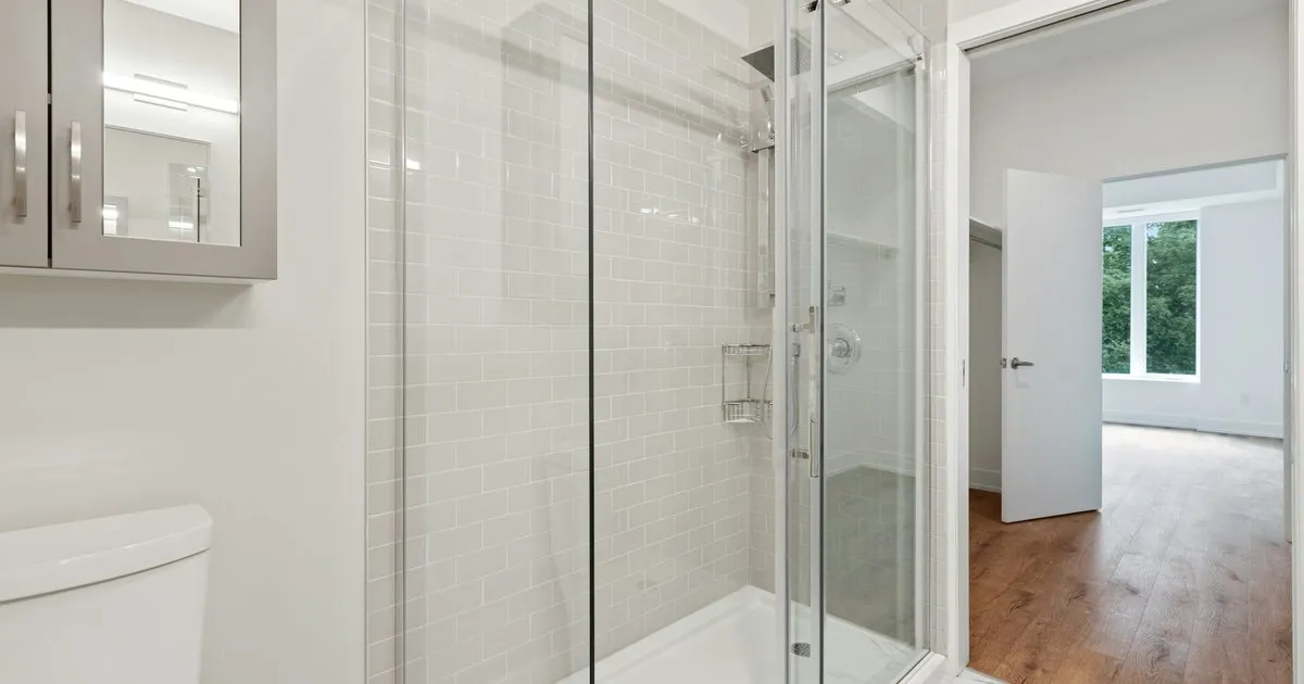 Ducha con división de vidrio templado corrediza de perfiles metálicos en un baño blanco con enchape tipo metro