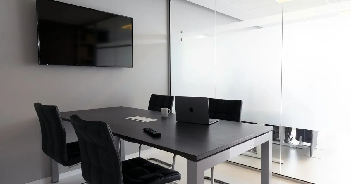 Sala de reuniones con divisiones de vidrio templado de piso a techo, mesa negra y pantalla en el muro