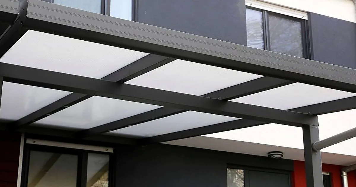 Marquesina de estructura metálica gris oscura con paneles traslúcidos blancos cubriendo la entrada de una casa moderna
