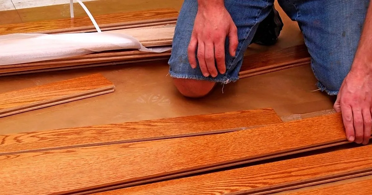 Instalador arrodillado ensamblando tablas machihembradas de madera en tono rojizo