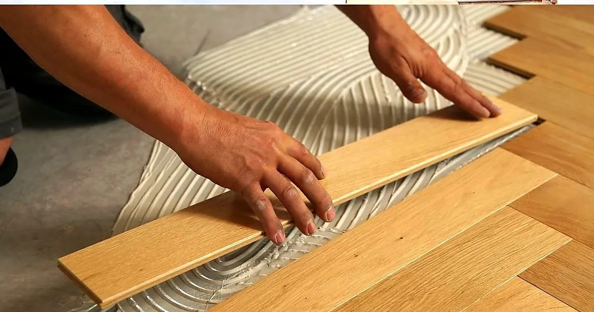 Manos de un instalador asentando una tablilla de parquet en espiga sobre adhesivo peinado con llana dentada