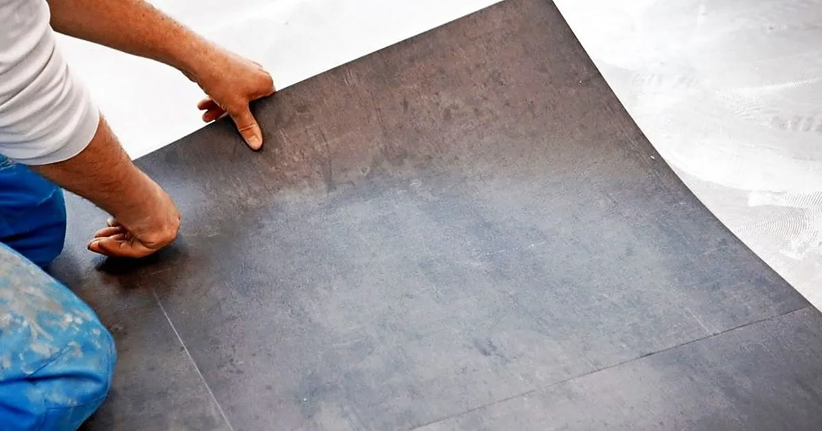 Instalador asentando con las manos una lámina flexible de piso vinílico gris oscuro sobre la base preparada