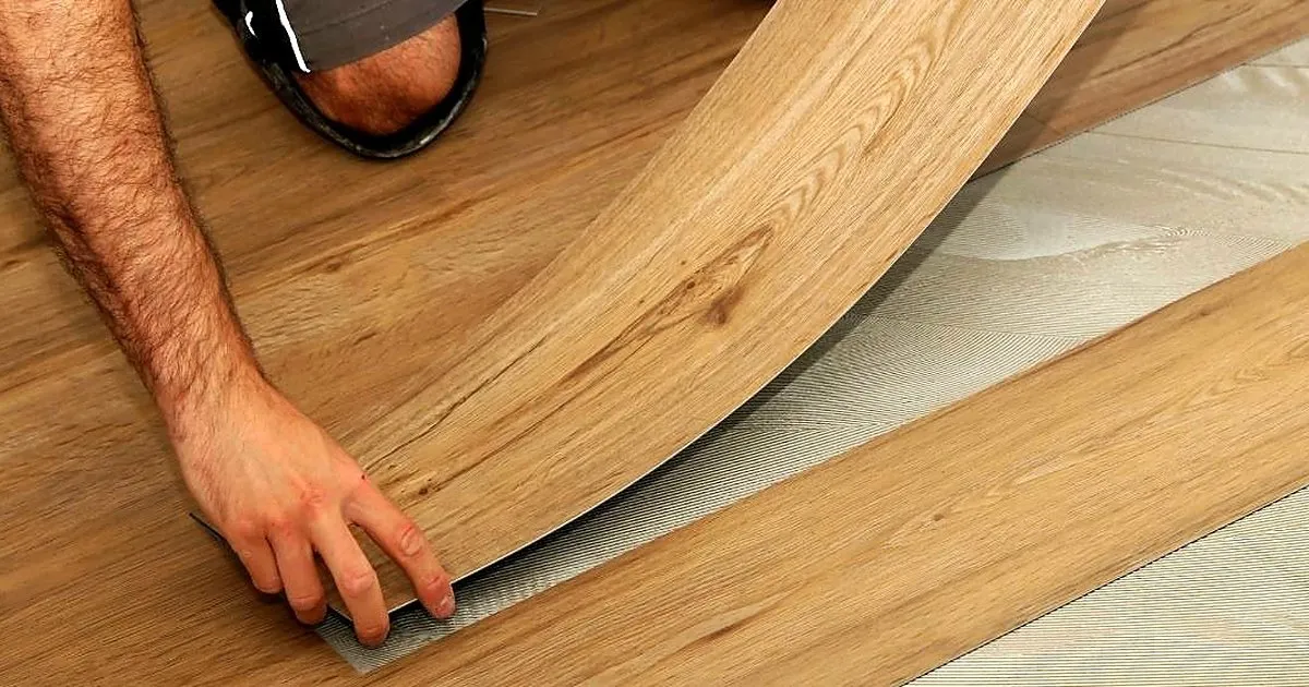 Manos de un instalador colocando un tablón flexible tipo madera en tono roble sobre la base preparada