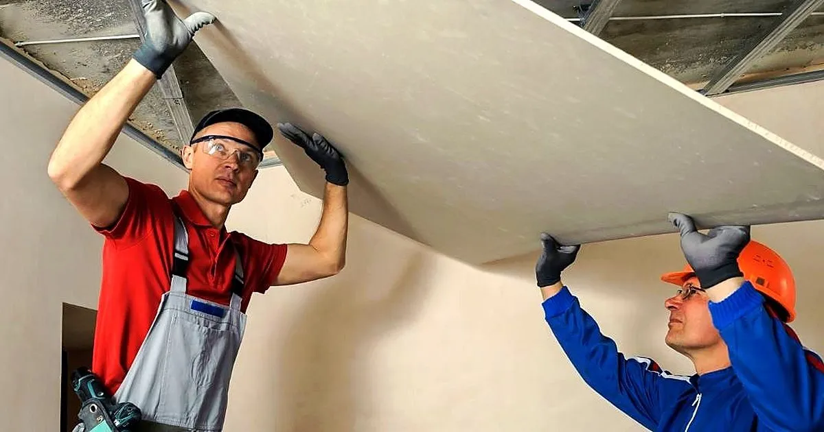 Dos instaladores sosteniendo una placa de drywall contra el techo mientras la fijan