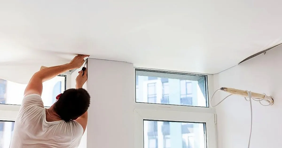 Instalador de espaldas rematando con espátula el borde de un cielo raso blanco junto a una columna y un ventanal