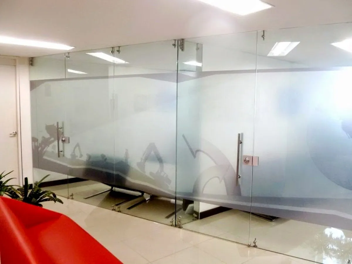 Divisiones de oficina en vidrio templado con película esmerilada decorativa, herrajes en acero y puertas batientes con manija tubular
