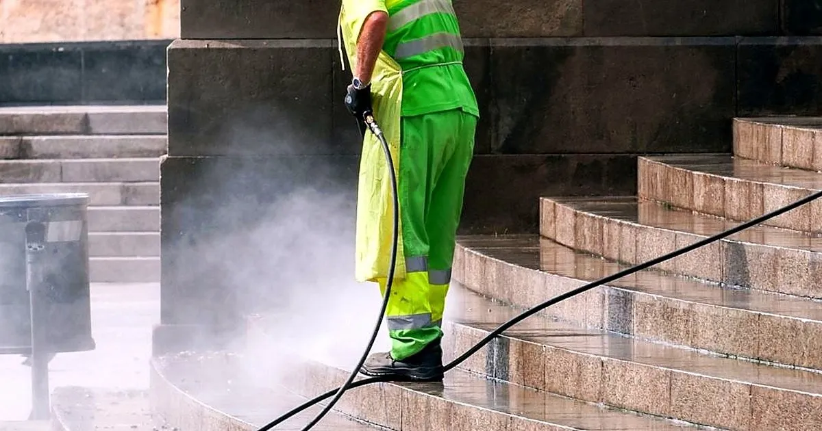 Operario con uniforme reflectivo lavando con hidrolavadora una escalinata exterior de piedra