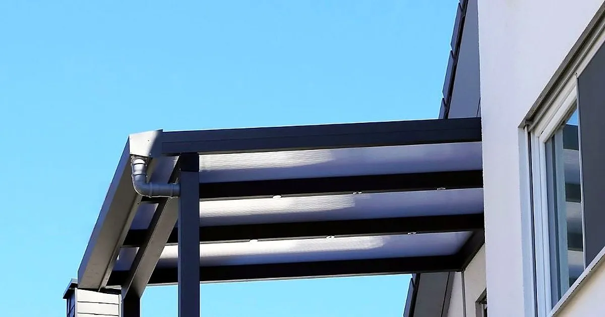 Marquesina de estructura metálica oscura con cubierta traslúcida y bajante de agua, adosada a una fachada blanca