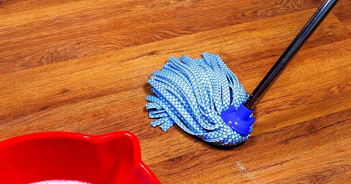 Trapero azul de tiras y balde rojo con espuma sobre un piso laminado de tono caoba