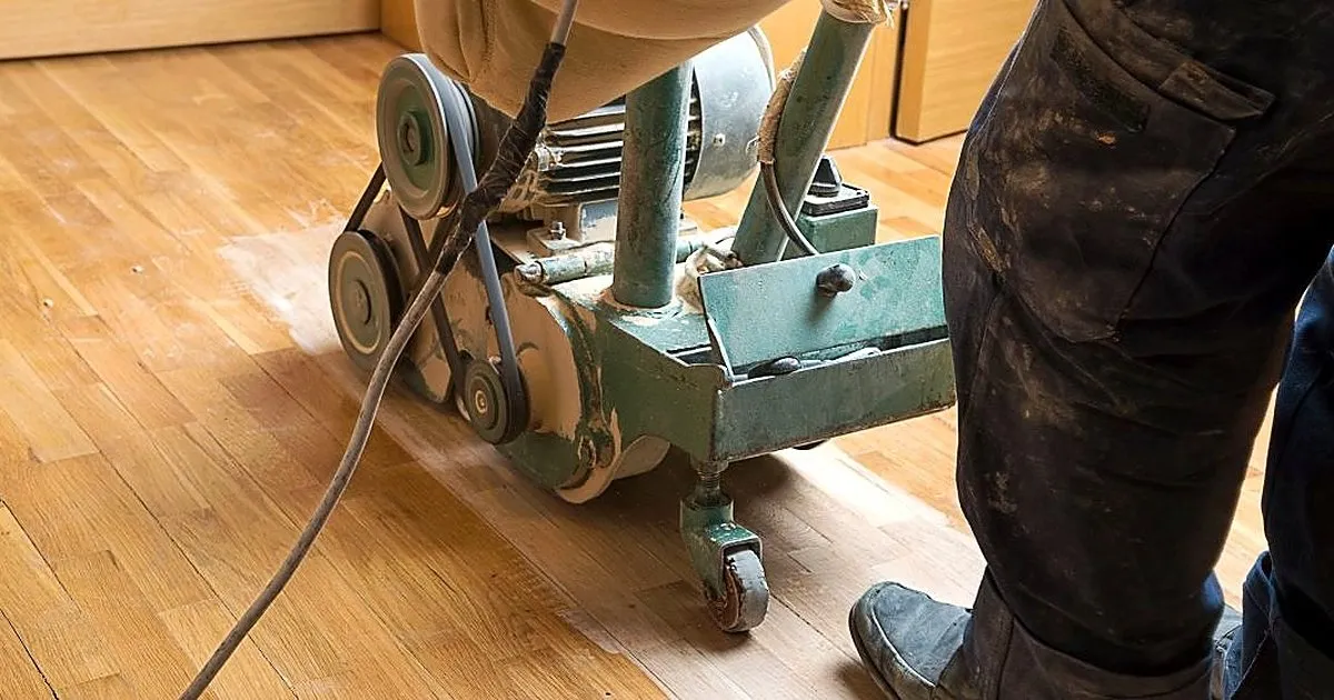 Operario manejando una lijadora de banda verde con bolsa recolectora sobre un piso de madera clara