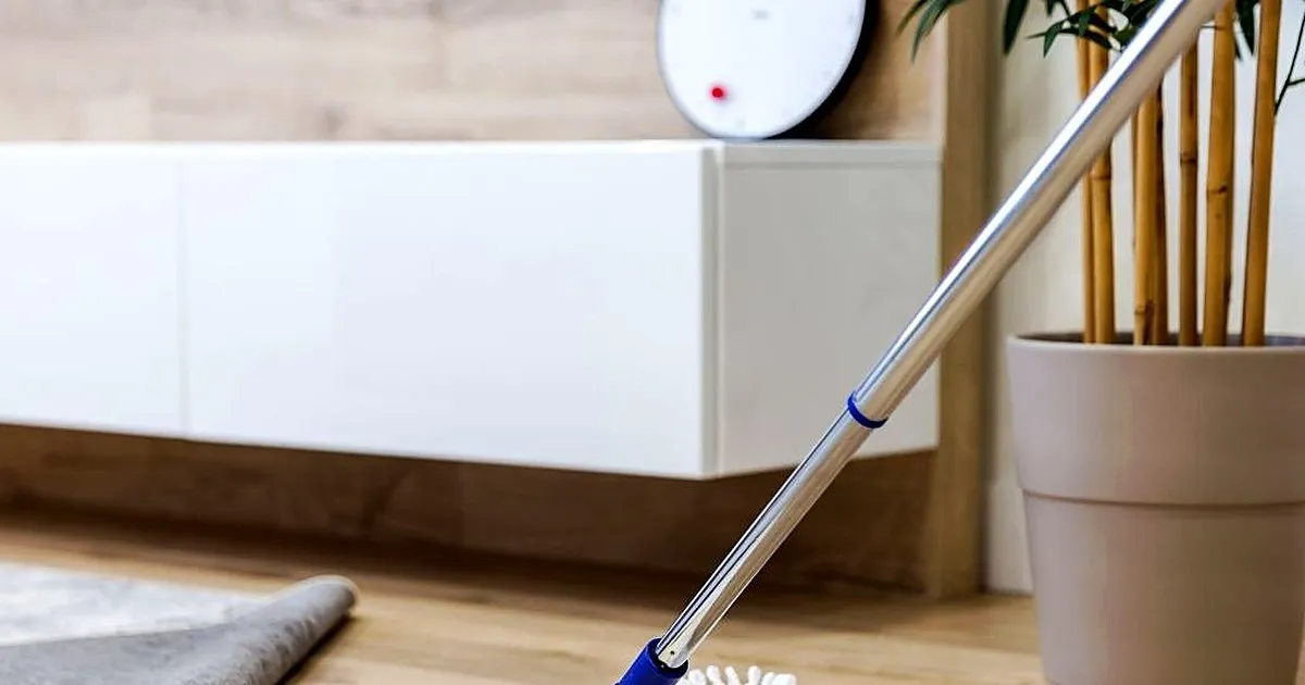 Mopa plana de microfibra limpiando un piso claro tipo madera junto a un mueble blanco flotante y una matera