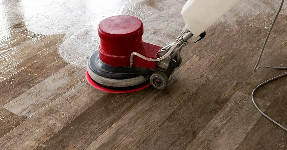 Máquina rotativa roja con pad suave lavando con espuma un piso de tablones tipo madera en tono gris