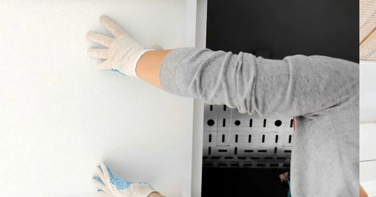 Manos con guantes presionando una lámina blanca de cielo raso contra el techo junto a una bandeja portacables perforada
