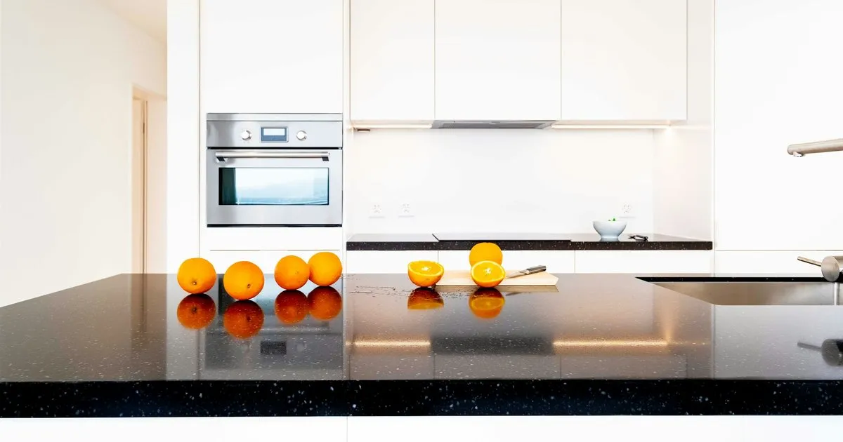Mesón de granito negro brillante con naranjas encima en una cocina de gabinetes blancos y horno empotrado