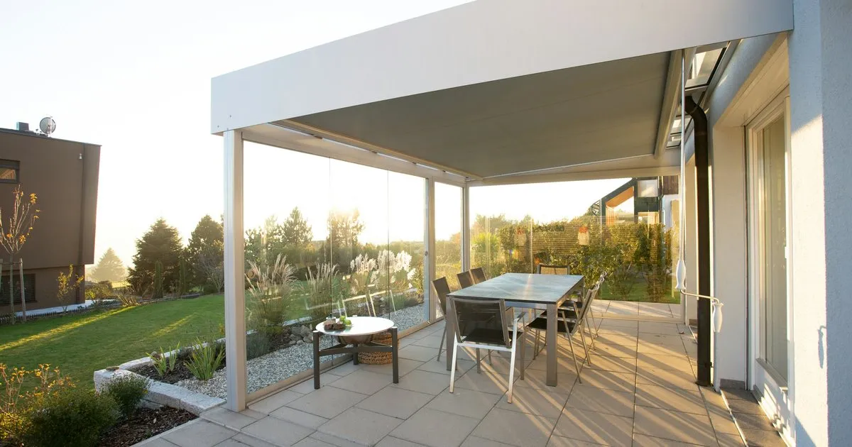Pérgola blanca adosada a la casa cubriendo un comedor exterior sobre piso de baldosa