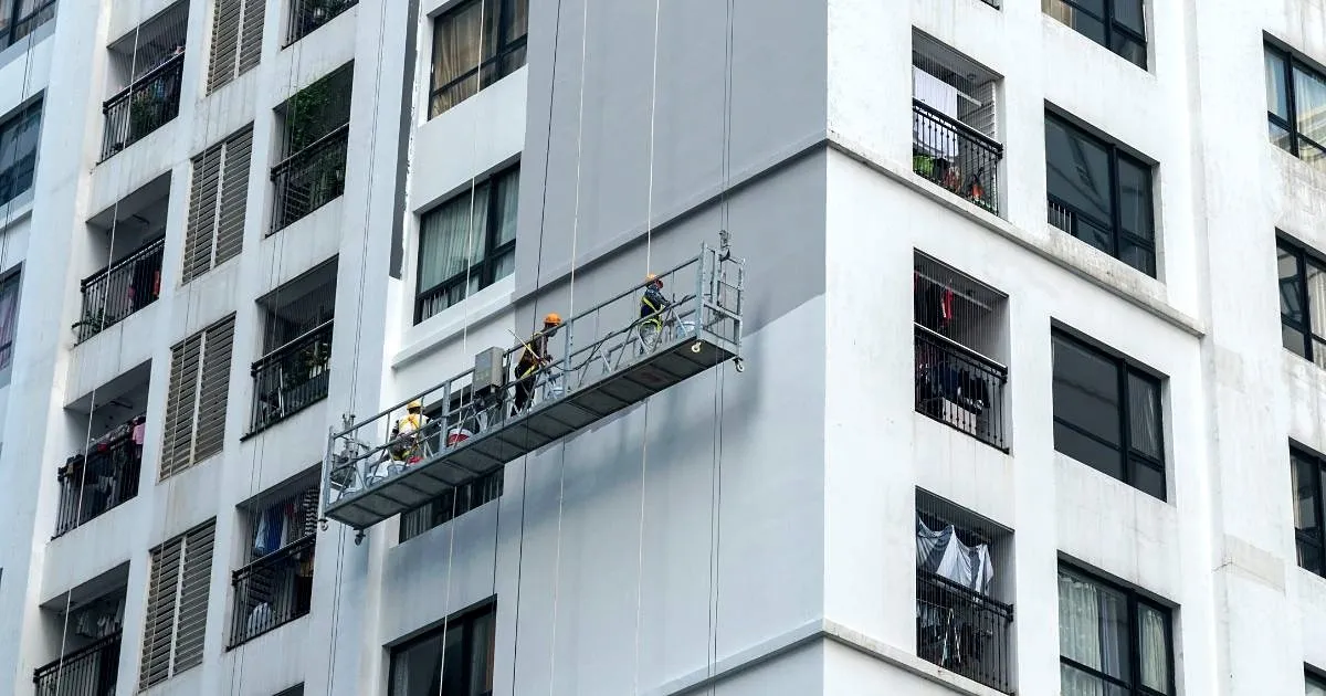 Andamio colgante con operarios trabajando sobre la fachada blanca de un edificio de apartamentos de varios pisos