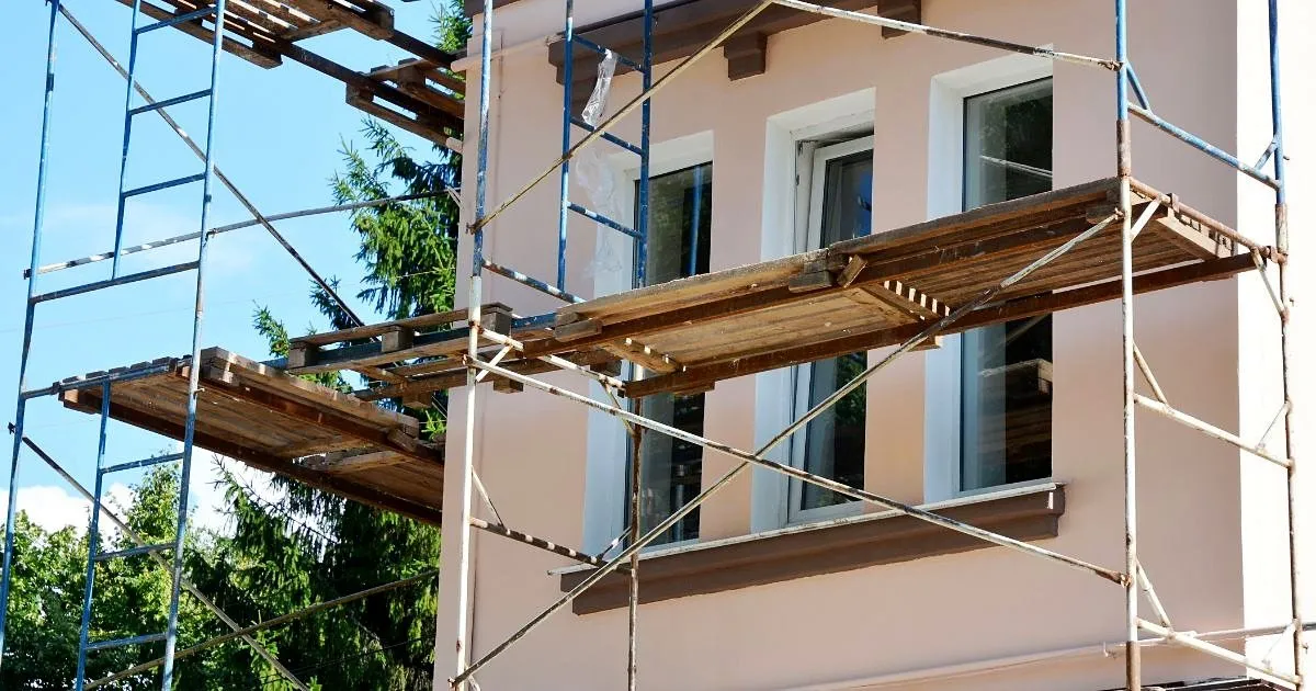 Fachada de una casa de dos pisos color salmón con andamio tubular y plataformas de madera