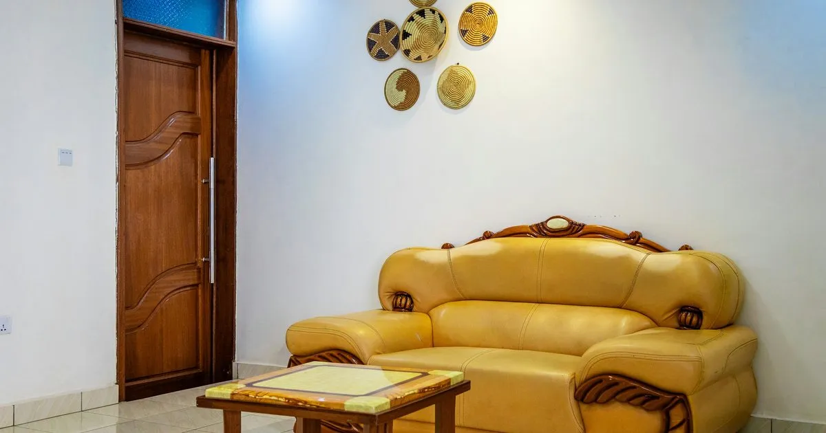 Puerta de madera maciza tallada con tirador metálico vertical en la entrada de una sala con un sofá amarillo