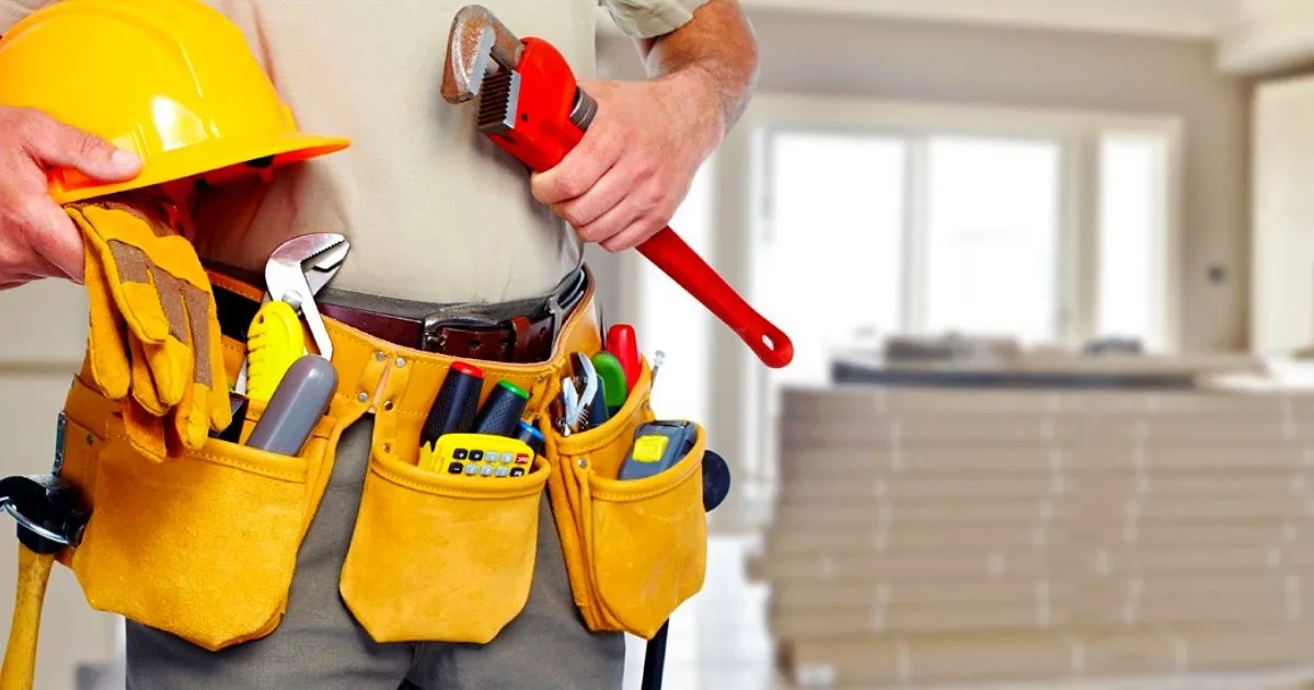 Trabajador con cinturón de herramientas amarillo sosteniendo un casco y una llave de tubo roja