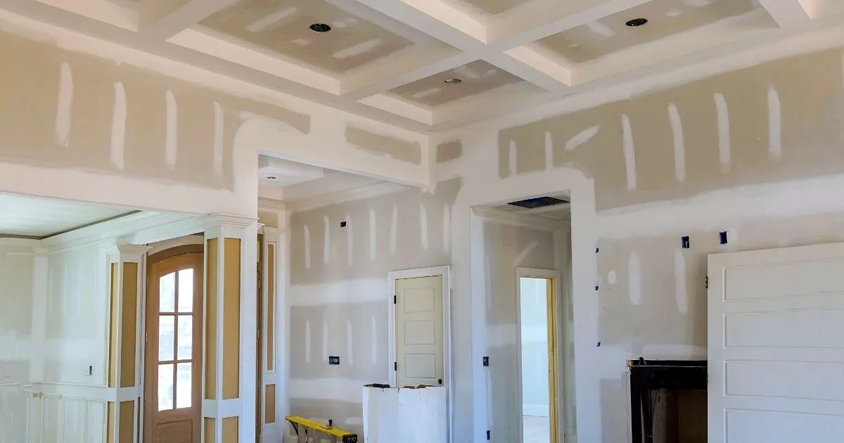 Interior de una casa en remodelación con muros y cielorraso artesonado en drywall con juntas masilladas y puerta de madera al fondo