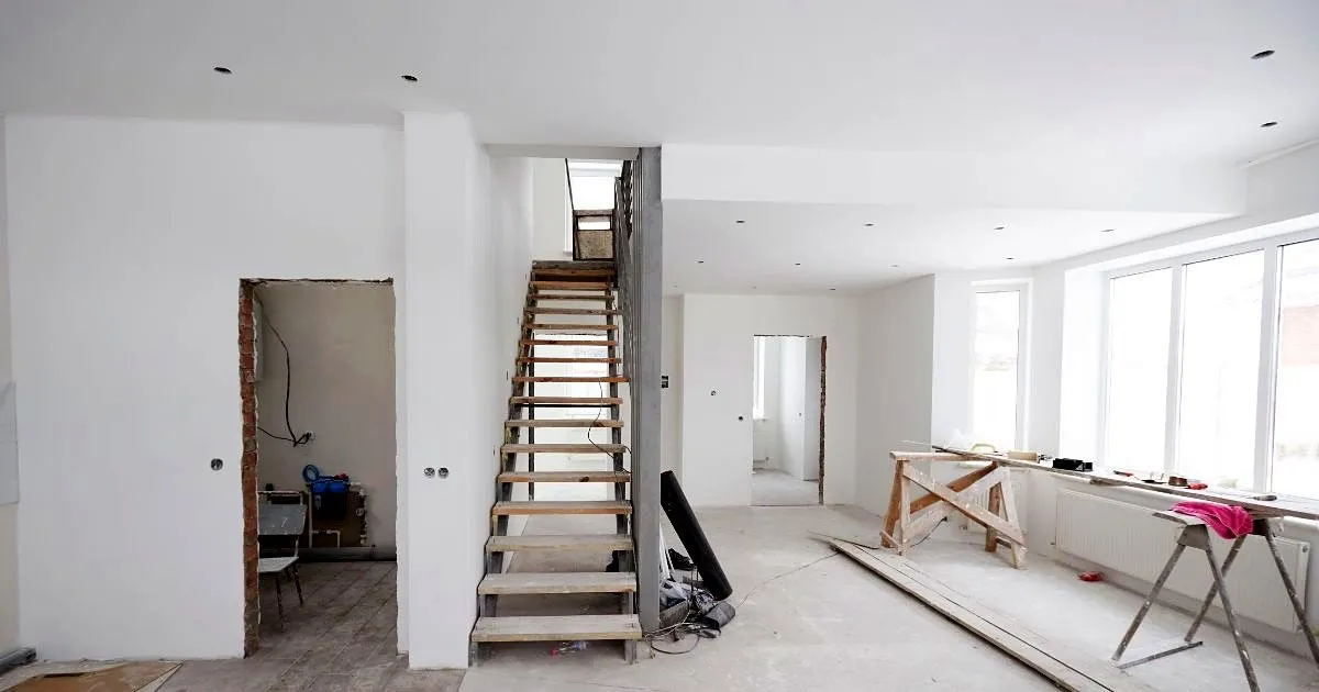 Primer nivel de un dúplex en obra blanca con escalera de estructura metálica y pasos de madera provisionales, luces empotradas y ventanal amplio