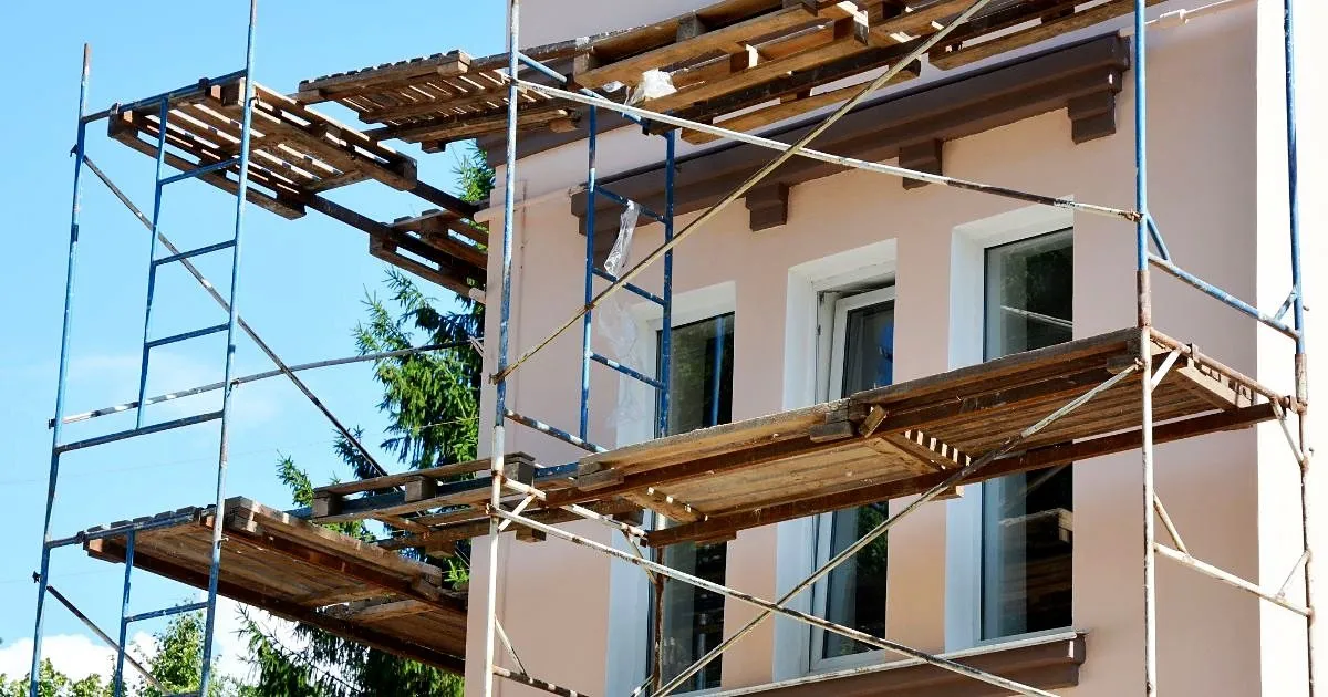 Fachada de una casa de dos pisos en tono salmón con andamios metálicos y plataformas de madera durante su remodelación