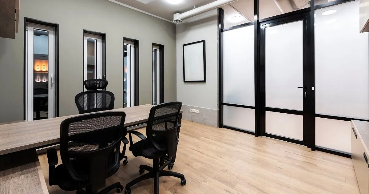 Sala de juntas remodelada con mesa larga, sillas ergonómicas negras, piso tipo madera y divisiones de vidrio esmerilado con perfiles negros