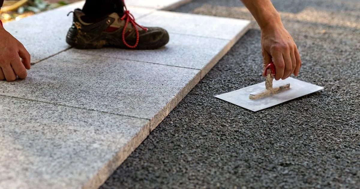 Instalación de losetas de piedra gris sobre una base de gravilla, con llana y bota de trabajo en primer plano