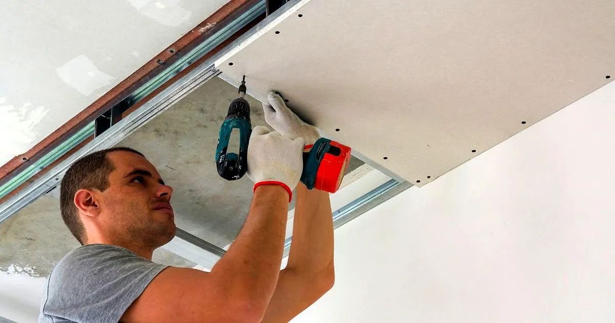 Técnico atornillando con taladro una lámina de drywall a la estructura metálica de un techo