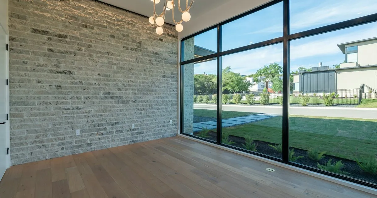 Ventanal de piso a techo con perfilería de aluminio negro en una sala con muro de piedra y piso de madera